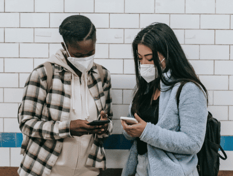 Two people with backpacks on looking at their cell phone