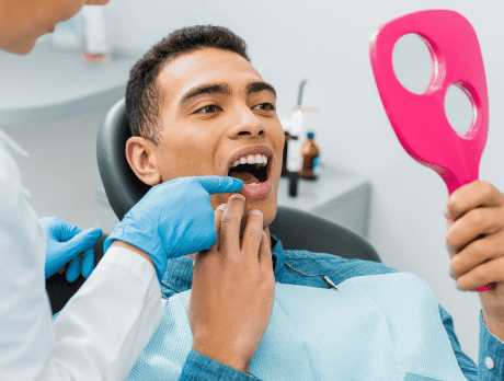 Homem no dentista segurando um espelho para olhar seus dentes