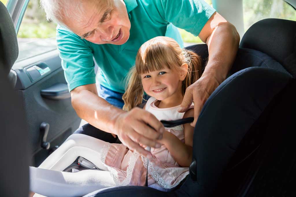 Grandparent-buckling-child-into-car-seat-as-caregiver