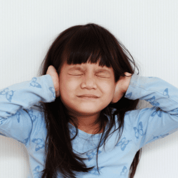 A distressed child holding her hands over her ears