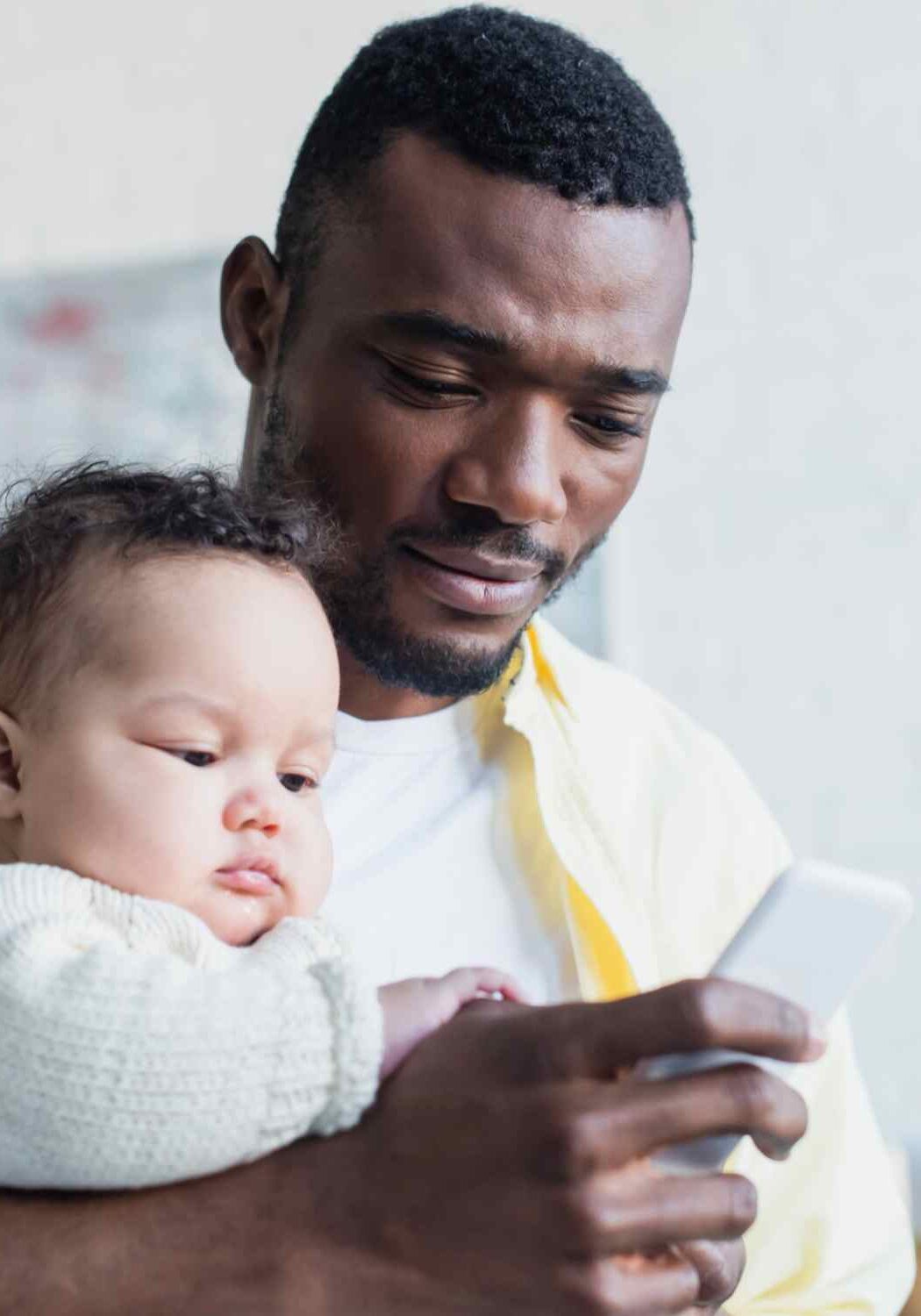赤ちゃんを抱きながら携帯電話でメッセージを打つ父親